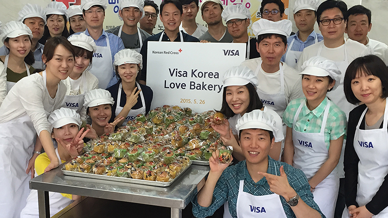 Sign of Korean Red Cross, Visa, Visa Korea Love Bakery, May 26, 2015, with bakers and goods gathered around signs. 