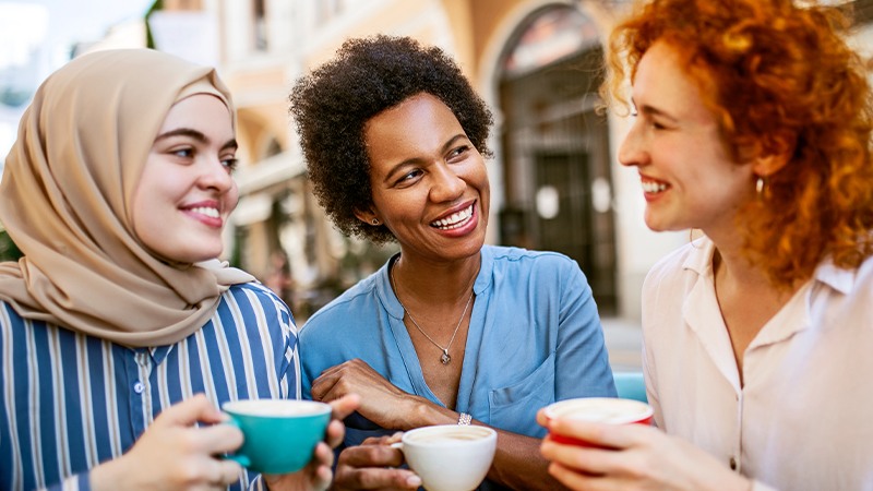 Three women of different nationalities and religion views laughing and having tea together